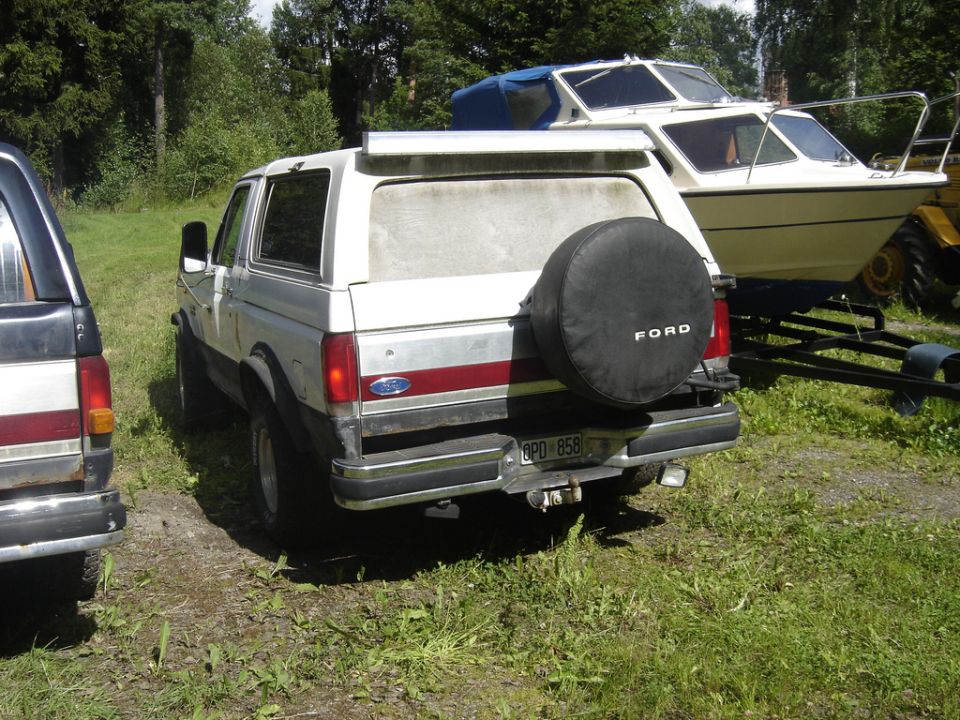 Rear of a white Ford pickup with spare tire cover by a boat