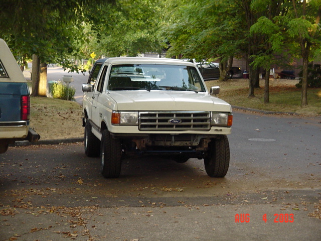 White lifted Ford pickup parked in a leaf-strewn driveway with front bumper removed