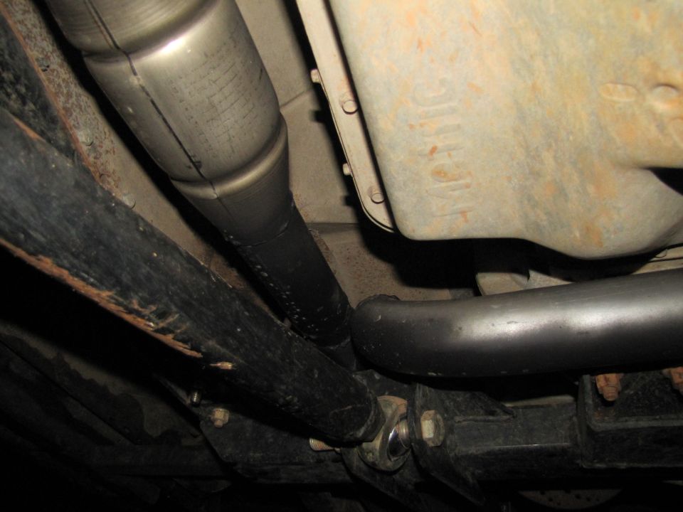 Undercarriage view of vehicle parts including exhaust pipe, drive shaft, and transmission housing with visible text