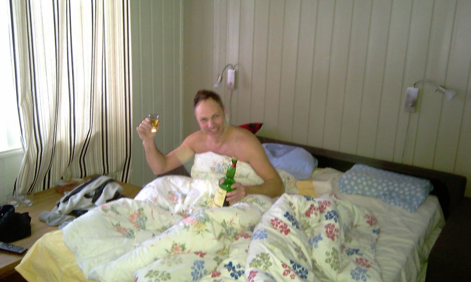 Man in bed holding a drink and a wine bottle