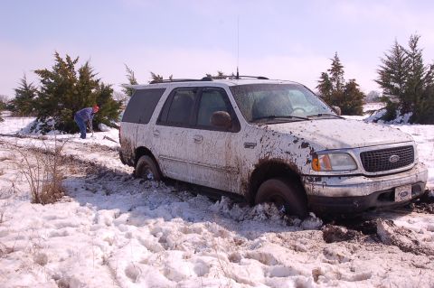 2002 Ford Expedition - A white 2002 Ford Expedition is stuck in a snowy and muddy field, with a person attempting to dig it out.