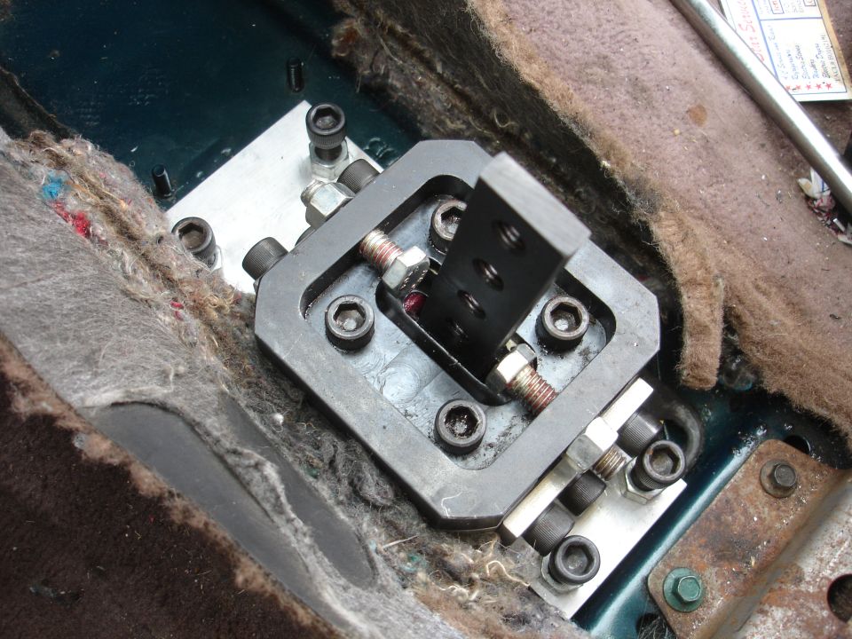 Aftermarket short shifter mechanism installed in a vehicle interior, with exposed carpet and metal components