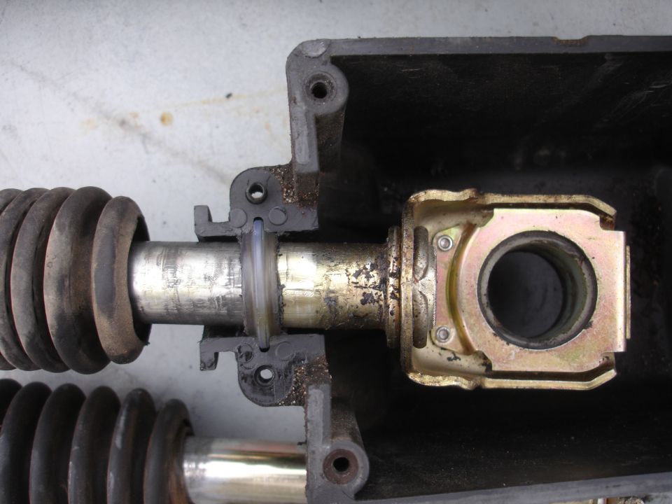 Close-up of a metal shaft with a rubber boot, connected to a gold-colored bracket with a circular opening
