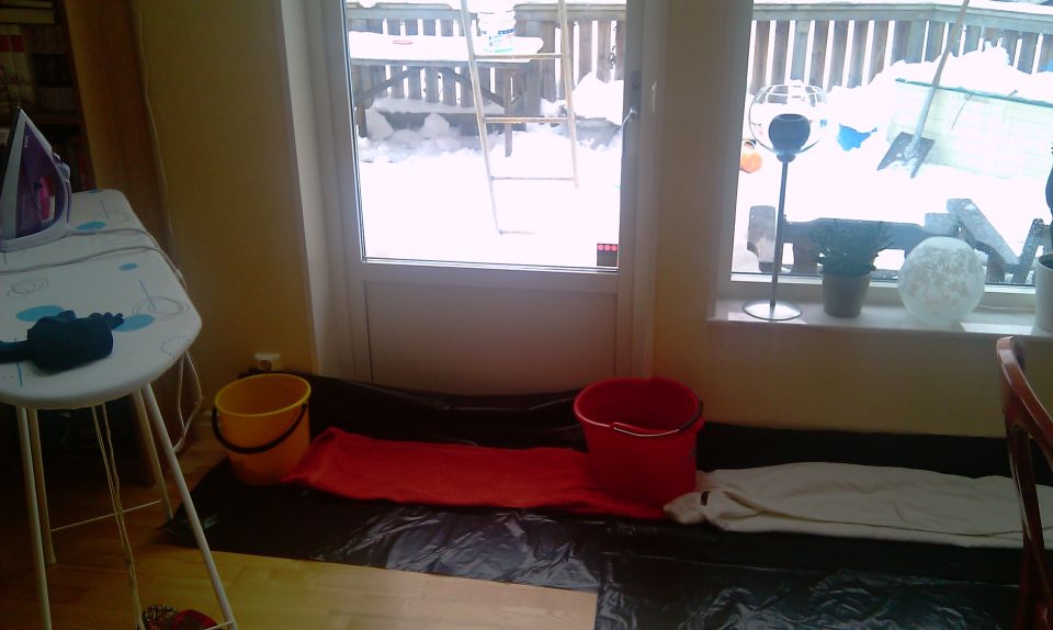 Home interior with buckets and plastic sheeting catching a leak by a snowy patio door