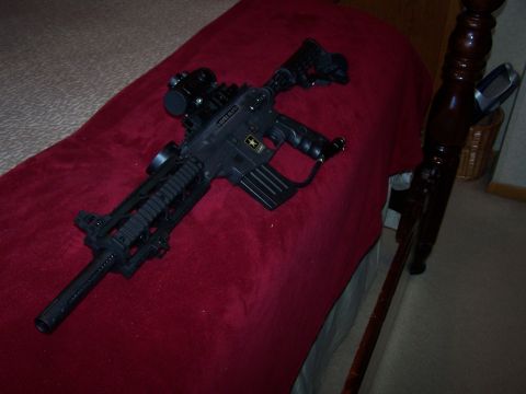 1986 Ford Bronco - A black paintball gun with tactical accessories is displayed on a red surface.
