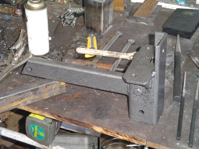 Black welded steel bracket with hex bolt on a cluttered workshop bench among tools
