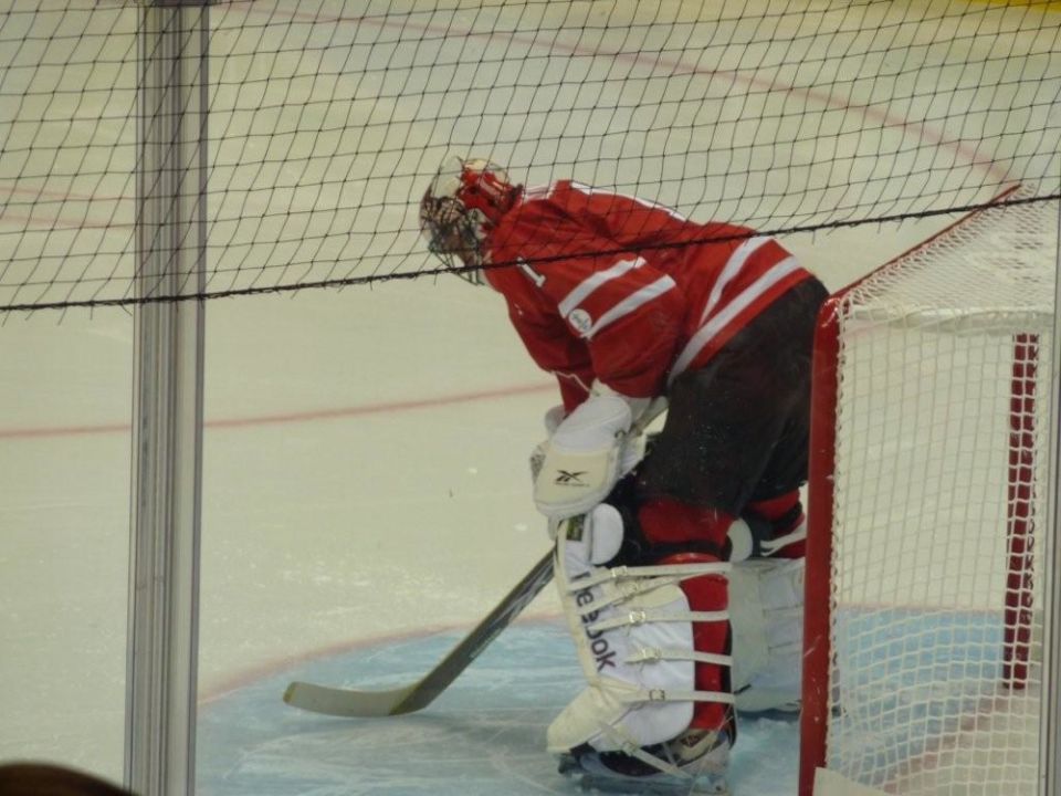 Hockey goalie in red uniform bent over with stick