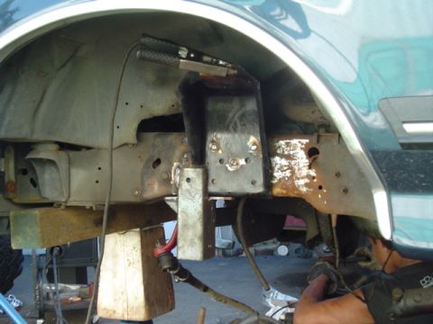 1993 Ford Bronco - Underside view of a vehicle's front wheel well area with the tire removed, showing bare metal frame brackets, welded steel plates, and surf…