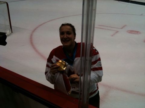 1996 Ford Bronco - A smiling woman in a red and white hockey jersey holds a gold medal on an ice rink.