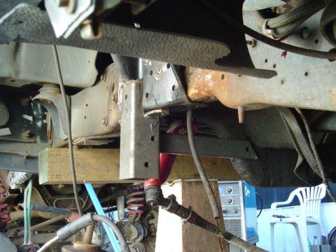 1993 Ford Bronco - Underbody view of a lifted truck's frame rail and body mount area, showing a fabricated steel bracket bolted to the frame, surface rust on…