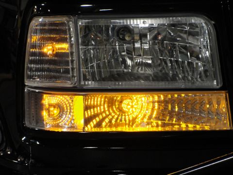 1995 Ford Bronco - Close-up of the front corner of a black 1995 Ford Bronco, highlighting the illuminated amber turn signal and clear headlight assembly.