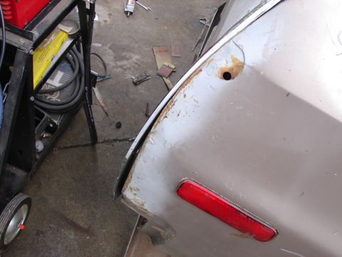 1973 Ford Ranchero - Detail of a vehicle's rear quarter panel showing rust and a red reflector, possibly undergoing repairs.