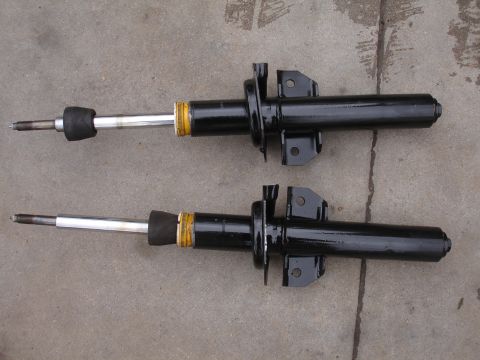 1995 Ford Taurus - Two black shock absorbers are shown from a side angle, resting on a gray concrete surface.