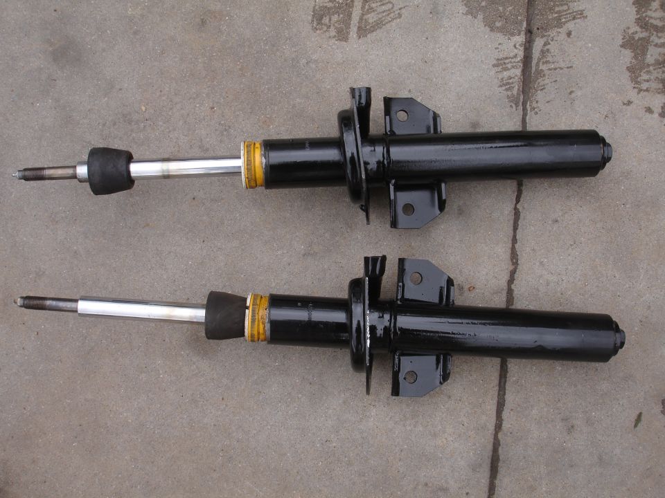 Pair of black shock absorbers with yellow bands and silver shafts, resting on a concrete surface