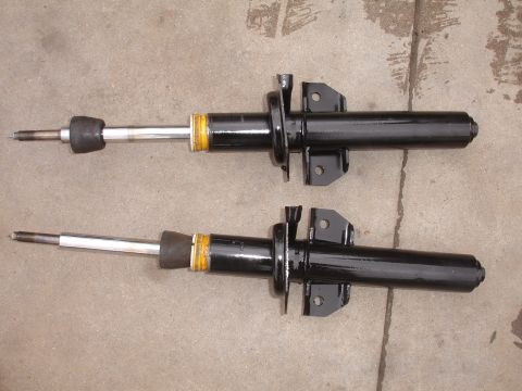 1995 Ford Taurus - Two black front shock absorbers with yellow bands and silver shafts are displayed on a concrete surface.