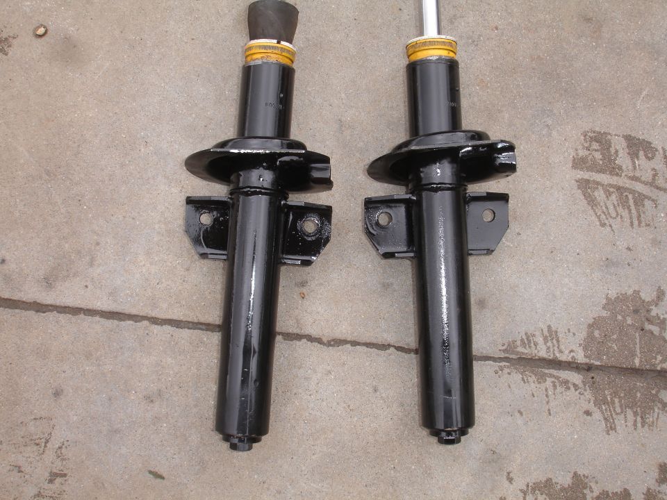 Two black shock absorbers with yellow top mounts and black rubber boots