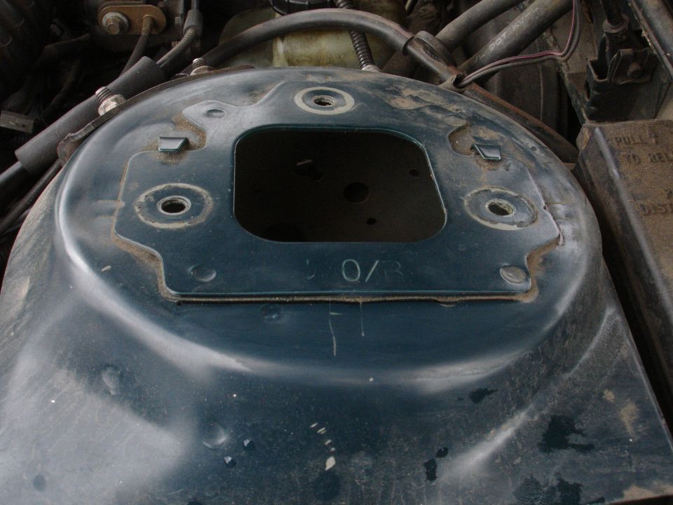 Close-up of a car's engine bay strut tower with a square opening and some markings