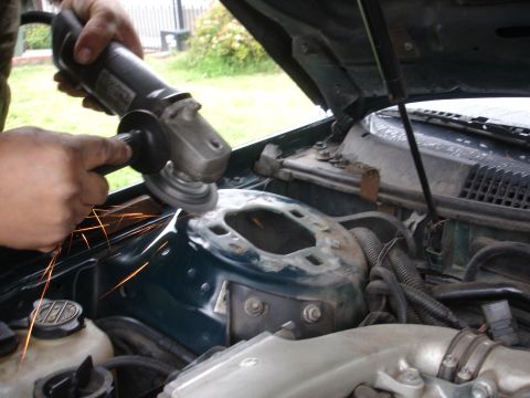 1995 Ford Taurus - An angle grinder is used to cut into the strut tower of a vehicle's engine bay.