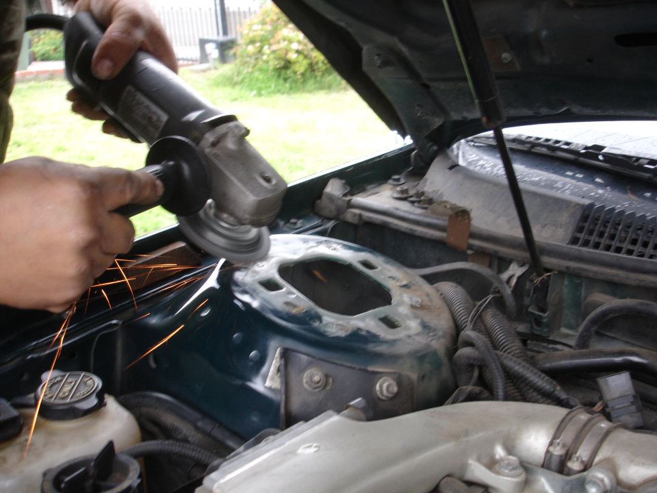 Green engine bay with an angle grinder cutting into the strut tower, sparks flying