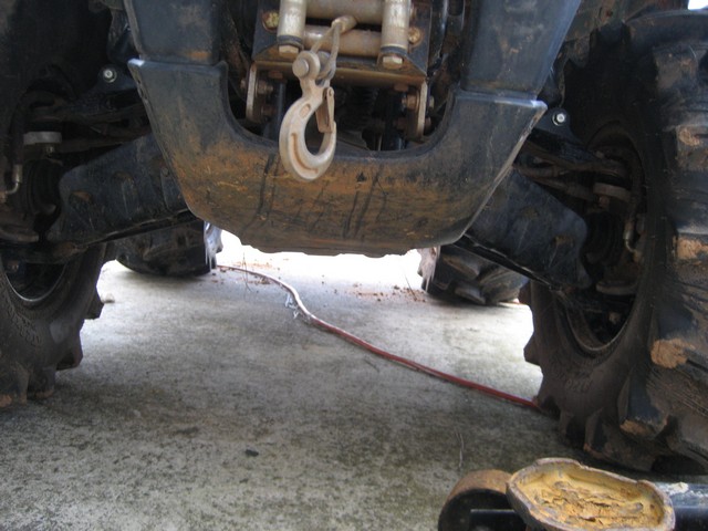 Underside of an ATV showing the winch, hook, and front suspension. A red cable runs across the ground