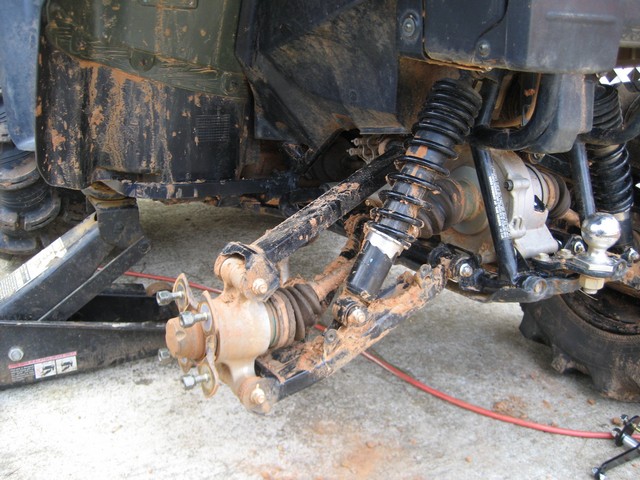 Close-up of ATV rear suspension and hitch assembly, with one wheel removed and a jack underneath