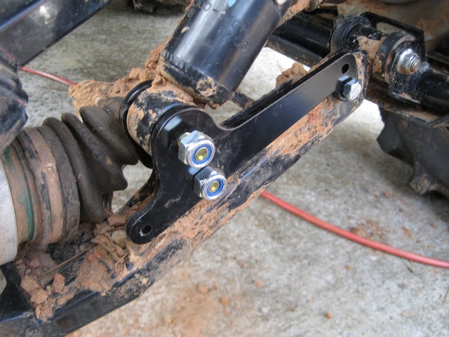 Black lift bracket bolted to muddy ATV rear trailing arm and shock mount