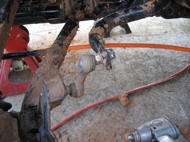 Mud-covered suspension linkage and frame components, with a red jack stand visible