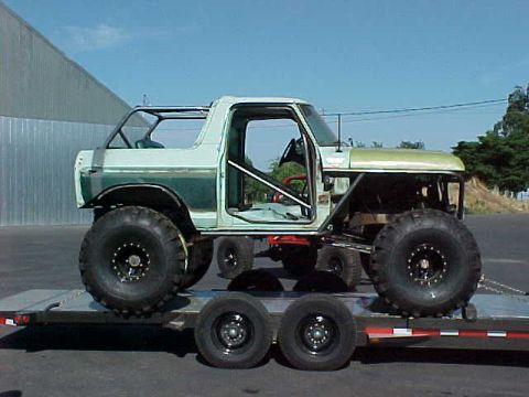2002 Ford F-350 - A heavily modified off-road truck with oversized tires is transported on a flatbed trailer.