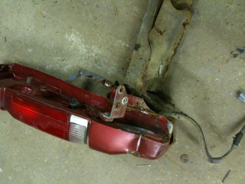 1993 Ford Bronco - A detached red taillight assembly and rusted metal bracket lie on a concrete surface.