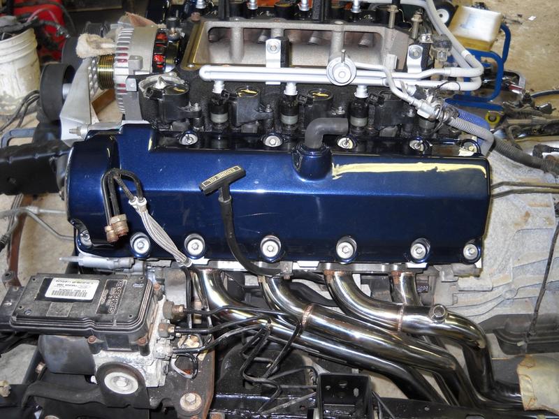 Blue engine with chrome exhaust headers and black intake manifold. Oil dipstick visible