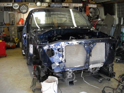 2007 Ford Mustang - Vehicle chassis undergoing disassembly in a garage setting, with the front end stripped bare.