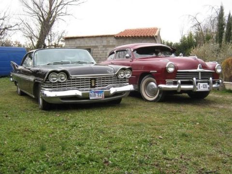 1991 Ford Crown Victoria - Two classic cars, a black Plymouth and a red Hudson, are parked side-by-side on a grassy lawn.