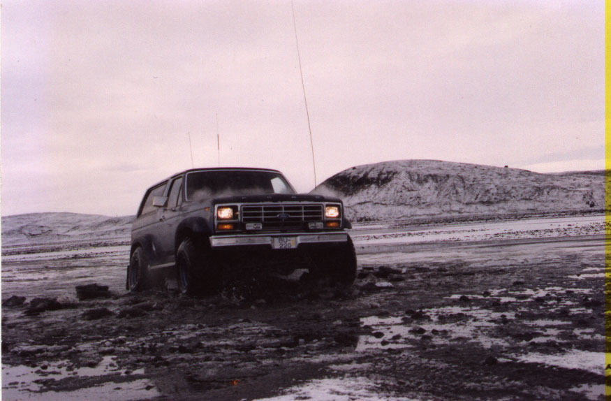 Dark full-size SUV front 3/4 view in muddy snowy terrain with antennas raised.