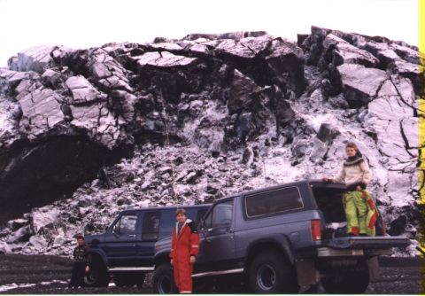 1986 Ford Bronco - Two SUVs and people are positioned in front of a massive rock formation.