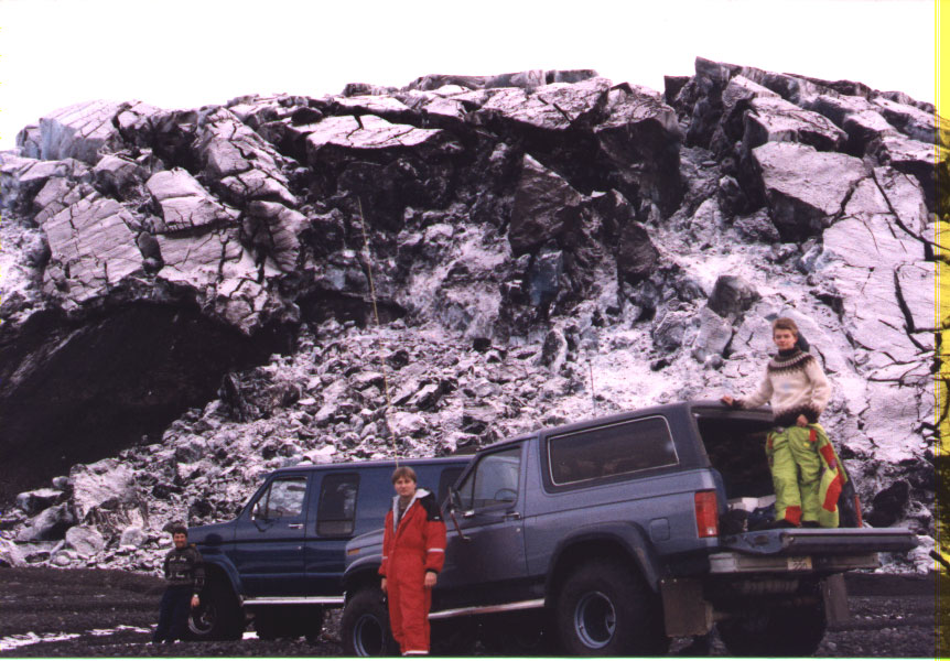 Two SUVs parked in front of a large rock formation. People stand near the vehicles