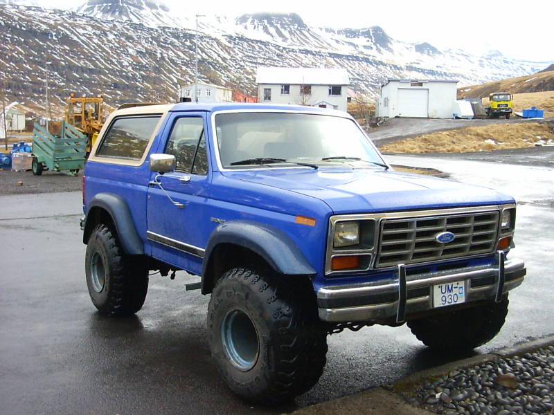 Blue Ford Bronco with large tires and a tan top, parked on a wet road