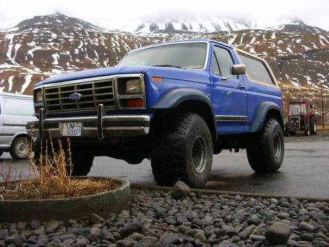 1986 Ford Bronco - This blue Ford Bronco is parked in front of a rocky area with snowy mountains in the distance.