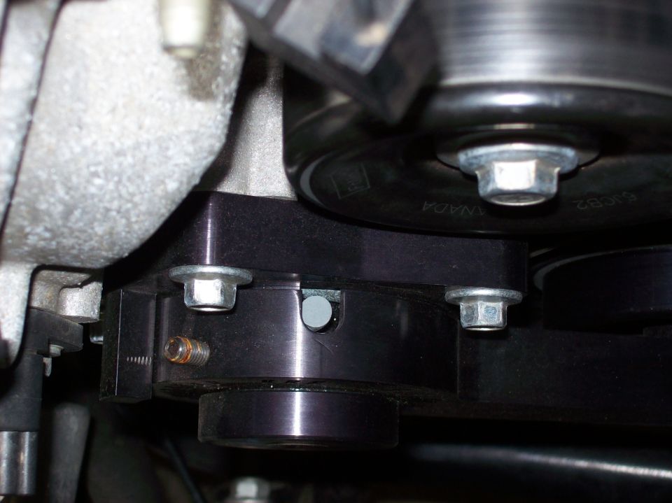 Close-up of an engine belt tensioner pulley assembly with bolts and a belt