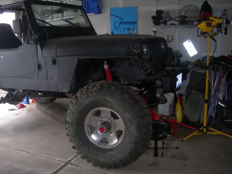 1991 Jeep Wrangler - A black Jeep Wrangler with oversized tires and red suspension components is shown in a garage setting.