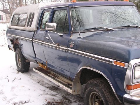 1979 Ford F-150 - This 1979 Ford F-150 pickup truck, equipped with a camper shell, shows considerable rust damage on its lower body and running boards.