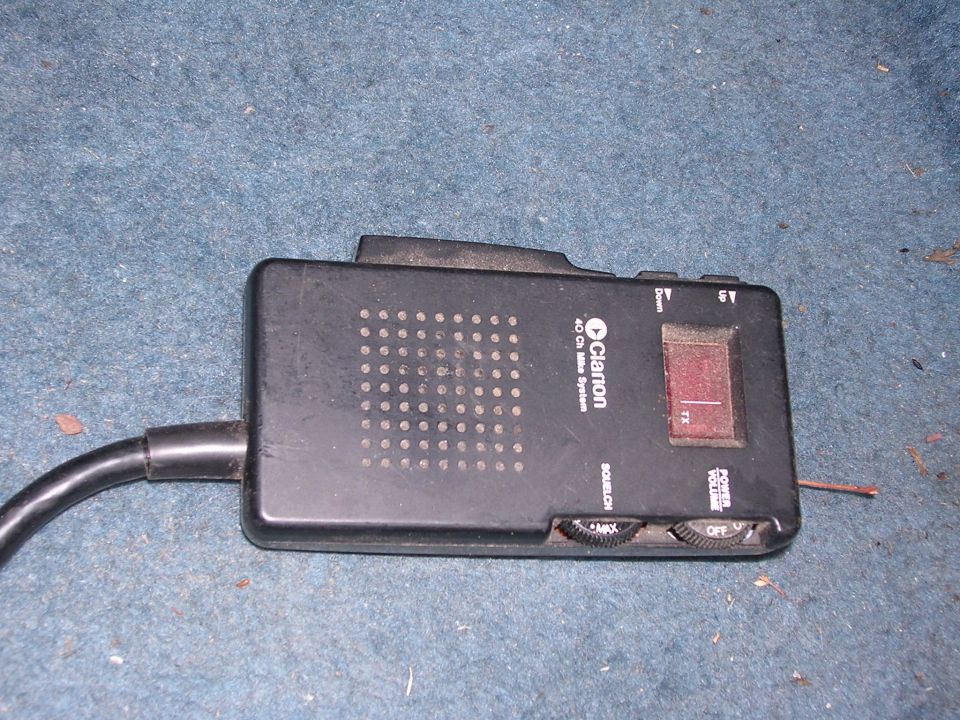 Black Clarion CB radio with red transmit button and volume knobs on blue carpet