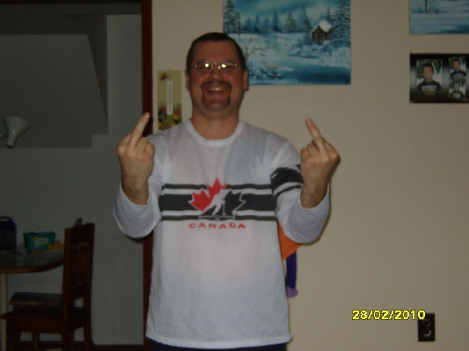 Man in a white shirt with a Canadian maple leaf design gives the middle finger with both hands