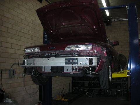 1992 Ford Crown Victoria - Front end of a maroon sedan is disassembled on a car lift in a garage.