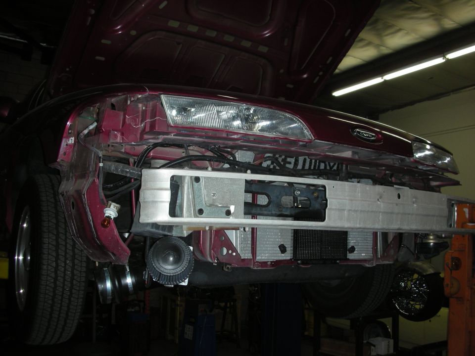 Car front end with hood up, bumper removed, showing intercooler and radiator. Maroon paint