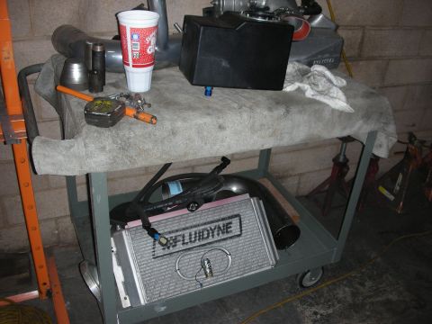 1992 Ford Crown Victoria - Various automotive parts, including an intercooler, are organized on a rolling cart.
