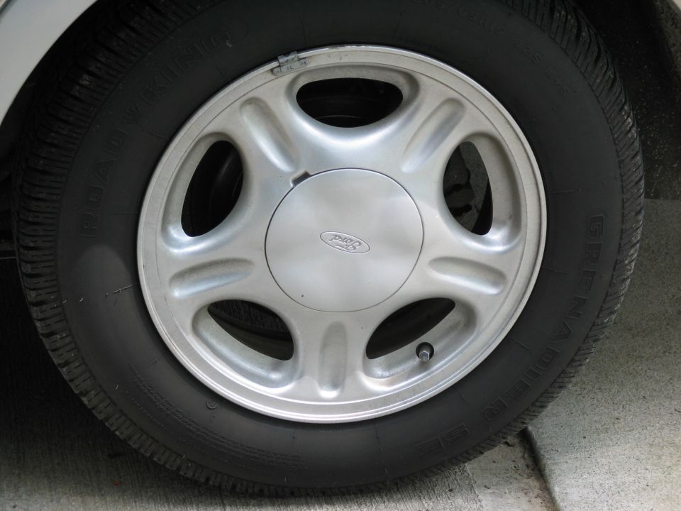 Ford five-spoke alloy wheel with center cap and Grenadier tire mounted on a silver vehicle