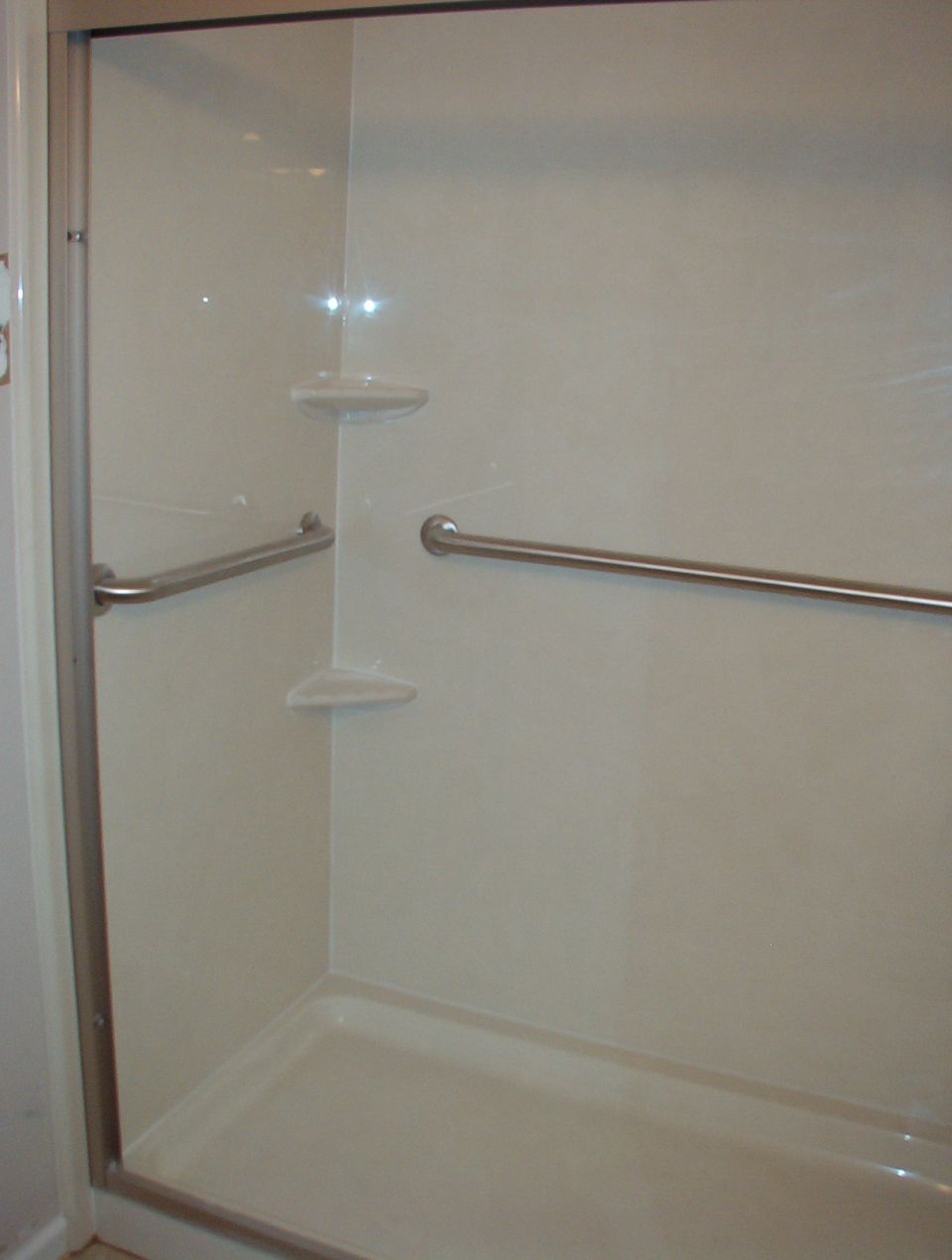 Cream shower enclosure interior with grab bars and molded corner shelves