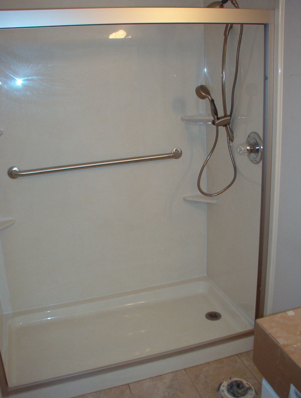 White fiberglass shower surround with grab bar and handheld sprayer in a bathroom remodel