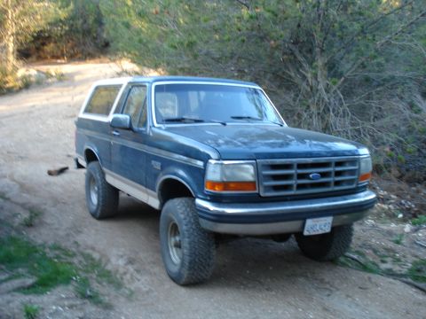 1993 Ford Bronco - This blue Ford Bronco is parked on a dirt road with trees in the background.