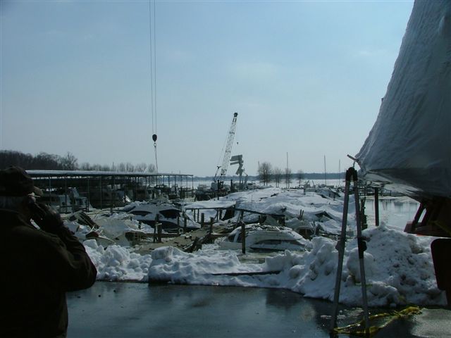 Collapsed snow-laden marina boat-slip roof crushing moored boats, crane working beyond